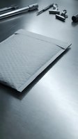 White bubble mailer envelope on metal surface with office tools in background. Shipping packaging concept for e-commerce business and postal services.