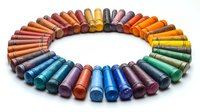 Colorful crayons arranged in rainbow circle pattern on white background, artistic composition showing spectrum of colors for drawing and coloring activities.