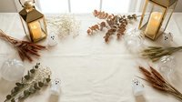 Cozy autumn flat lay with golden lanterns, dried eucalyptus branches, wheat stalks and white pumpkins on cream textured background for seasonal decor.