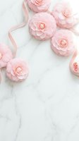 Pink camellia flowers with satin ribbon on white marble surface, elegant feminine flatlay for wedding, beauty, or lifestyle branding.
