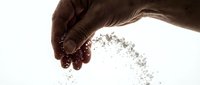 Hand pouring sand or granular material against white background, isolated for design use on merchandise and promotional materials.