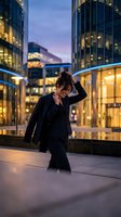 Stressed businesswoman holding head in hands walking through modern financial district at dusk with illuminated office buildings in background.