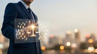 Professional businessman holding digital tablet displaying glowing justice scales with network connections against blurred city skyline at sunset.