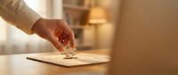 Person with medium skin tone placing a puzzle piece into a wooden puzzle on a table, symbolizing problem-solving and business strategy in a warm, professional office setting.