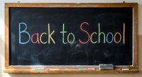 Colorful chalk text Back to School written on black chalkboard with wooden frame and chalk pieces for educational concepts and classroom designs.