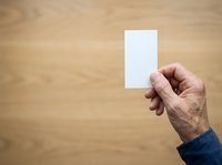 Hand holding blank white card against wooden background, suitable for business presentations, marketing mockups, and promotional designs.