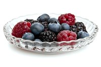 Fresh mixed berries including raspberries, blackberries and blueberries served in elegant crystal glass plate on white background, healthy natural dessert.