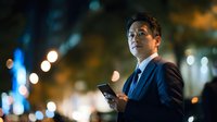 Professional Asian businessman in dark suit holding smartphone at night with blurred city lights background for corporate technology and business concepts.
