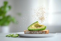 Sliced avocado on whole grain toast with cucumber and golden seasoning particles dispersing above, isolated on white plate for food styling and healthy eating content.