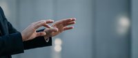 Professional businessman hands gesturing during presentation or speech in modern office environment with blurred background for corporate communication.