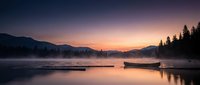 Serene mountain lake at dawn with wooden dock and boats, misty water surface reflecting purple pink sunrise sky, peaceful wilderness landscape for relaxation themes.