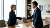Professional businesswoman and businessman shaking hands across conference table in modern office meeting room during successful negotiation.