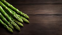 Fresh green asparagus spears arranged on dark wooden rustic background with copy space, top view. Natural organic vegetables for healthy cooking.