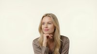Professional blonde businesswoman in brown blazer posing thoughtfully with hand under chin on neutral background for corporate marketing materials.