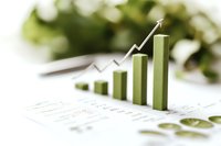 Green ascending bar graph with upward arrow showing positive growth trend on financial document with soft bokeh background and selective focus.