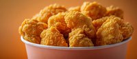 Crispy golden chicken nuggets in white paper container against warm orange background, popular fast food snack for menu advertising.