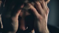Young Caucasian man covering face with hands expressing stress, anxiety, depression or emotional overwhelm in dark moody lighting for mental health concepts.