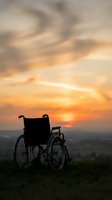 Empty wheelchair silhouetted against golden sunset sky with scenic landscape horizon, symbolizing hope, freedom, accessibility, and overcoming challenges in outdoor settings.