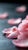 Delicate pink rose petals with morning dew drops scattered on dark textured surface, creating soft romantic mood in macro photography composition.
