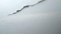 Close-up of a jagged crack running across a white textured wall surface, showing structural damage with soft focus background.