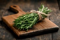 Fresh rosemary herb bunch tied with twine on rustic wooden cutting board against dark wooden background, aromatic cooking ingredient for culinary use.