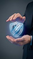 Businessman in dark suit holding glowing neon shield icon between hands, representing cybersecurity, data protection, and digital safety for business and technology concepts.