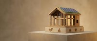Wooden house model with solar panels on roof sits on cardboard box with eco symbols, representing sustainable green energy and environmental construction.