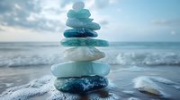 Stack of smooth sea glass stones balanced on beach with ocean waves and cloudy sky creating peaceful zen meditation scene for wellness and mindfulness concepts.