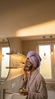 Young woman applying green facial mask in modern bathroom with cucumber slices for spa skincare routine and wellness relaxation at home.