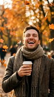 Happy young Caucasian man laughing with coffee cup in autumn park with falling leaves and warm golden bokeh light for seasonal lifestyle content.