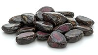 Polished garnet stones scattered on white surface showing deep red color and natural crystalline structure. Isolated mineral specimens for jewelry making and crystal healing.