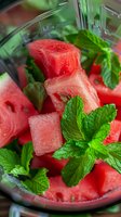 Fresh juicy watermelon cubes garnished with vibrant mint leaves in glass bowl, macro view showing texture and natural colors for summer refreshment.