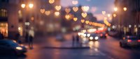 Blurred city street at night with heart-shaped bokeh lights creating romantic atmosphere. Urban evening scene with warm golden illumination and traffic.
