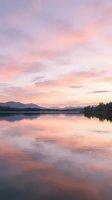 Serene lake landscape at sunrise with pink and orange sky reflecting on calm water, distant mountains, and forested shoreline for nature and travel projects.