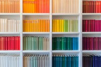 Colorful books arranged by spectrum colors on white bookshelf, creating rainbow pattern. Modern library interior with organized color-coded book collection.