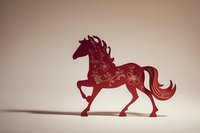 Red paper cut horse silhouette with floral pattern design, traditional Chinese zodiac symbol casting shadow on neutral background.