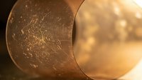 Golden copper pipe with water droplets and warm lighting creating industrial plumbing background for construction and engineering projects.