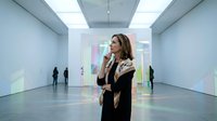 Young professional woman contemplating colorful digital art projections in modern gallery space with visitors exploring contemporary exhibitions.