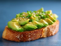 Fresh sliced avocado on toasted sourdough bread garnished with sesame seeds and microgreens against dark background, close up view of trendy breakfast.