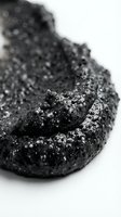 Macro shot of raw activated charcoal or black mineral specimen with crystalline texture and granular surface detail isolated on white background for design and educational use.