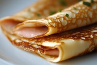 Freshly made thin crepes folded on white plate with delicate golden brown lacing pattern, close-up macro shot showing texture and layers of traditional pancakes.