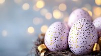 Pastel purple Easter eggs decorated with gold speckles and dots nestled in natural nest with golden ribbon against soft bokeh background. Holiday celebration concept.
