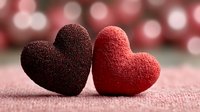 Two textured fabric hearts in burgundy and red colors on soft pink surface with romantic bokeh lights background for Valentine's Day celebration.
