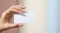 Close-up of a woman's hand holding a blank white business card against a soft gradient background with pink and blue tones. Perfect for branding and corporate presentations.