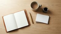 Minimalist workspace with open notebook, blank cards, wooden pen and coffee cup on natural wood desk for creative writing and planning projects.