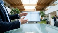 Professional businessman presenting data on tablet computer in modern office environment with natural lighting and contemporary architecture.