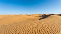 Golden sand dunes with rippled texture under clear blue sky, showcasing arid desert landscape with natural wave patterns and shadows for travel and nature backgrounds.