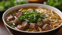 Asian beef noodle soup with meatballs, fresh herbs and broth in ceramic bowl. Traditional comfort food for restaurant menus and culinary content.
