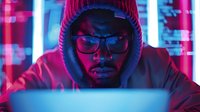 Young African American male programmer in glasses and red beanie working late at night on laptop, illuminated by vibrant neon lights creating cyberpunk atmosphere.