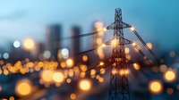 High voltage power line tower silhouette against blurred urban cityscape with glowing bokeh lights at dusk, modern energy infrastructure and electricity supply concept.